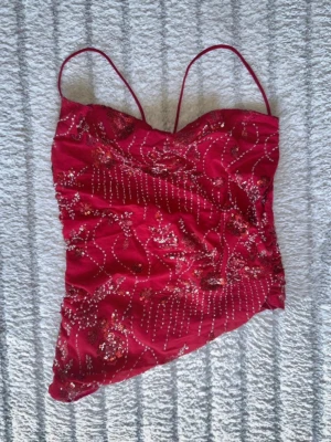 Röd paljettprydd linne S topp Ny! - Strl: S. Helt ny och oanvänd. Supersnygg röd linnetopp med tunna axelband och massor av paljetter och broderade detaljer i blommönster. Toppen har en lätt glittrig look och är perfekt för dig som vill sticka ut. Materialet känns lätt och svalt, och toppen har en dragkedja i sidan för enkel påklädning.