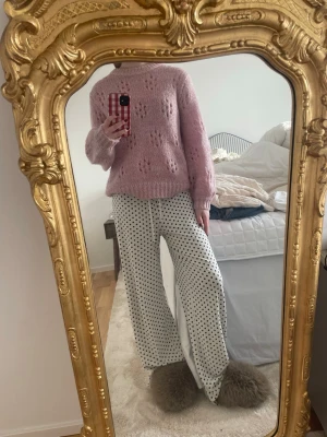 Ljusrosa stickad tröja med hålmönster - Mysig ljusrosa stickad tröja med blommigt hålmönster och ribbade muddar vid ärmslut och nederkant. Tröjan har en avslappnad passform och rund halsringning. Perfekt för dig som gillar en söt och trendig look.