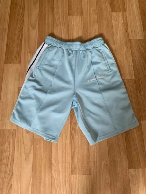 Palm Angels shorts - Snygga ljusblå shorts från Palm Angels med vita och svarta ränder längs sidorna. Shortsen har elastisk midja och sidofickor.