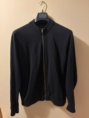 Massimo Dutti Zip Cardigan i 100% Merinoull - Massimo Dutti Zip Cardigan i 100% Merinoull  Stilren och tidlös mörkblå cardigan från Massimo Dutti, tillverkad i exklusiv 100% merinoull. Ett högkvalitativt plagg som är mjukt, bekvämt och passar lika bra till jeans som över en skjorta. Mycket fint skick och perfekt för dig som uppskattar klassisk stil och premiumkvalitet. En garderobsfavorit som aldrig går ur tiden.