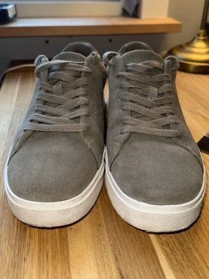 Grå mockasneakers med snörning - Snygga gråish sneakers i mocka med klassisk design och vita sulor. Skorna har matchande grå snörning och en stilren look som passar till det mesta. Perfekta för dig som gillar enkel och clean stil. Pris kan diskuteras vid snabb affär