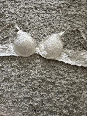 Vit spets-bh Lindex - Säljer en elegant vit bh med vadderade kupor och fina spetsdetaljer över hela bh:n. Axelbanden är justerbara och bh:n har hakknäppning bak. Perfekt för dig som gillar romantisk och feminin stil.
