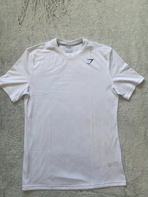 Vit t-shirt(slim-fit) från Gymshark - Säljer en stilren vit t-shirt från Gymshark med diskret logga på bröstet. Den är slim-fit! Helt ny och knappt använd! Fråga vid pris eller frågor! Förpackningen skickas med! 