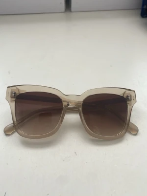 Beige solglasögon från CHIMI - Snygga solglasögon från CHIMI med transparent beige båge och fyrkantig form. Glasen är bruna med en snygg toning. Perfekta för att lyfta din stil under soliga dagar.