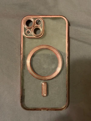 Transparent mobilskal med roséguld-detaljer - iPhone 15 skal Snyggt transparent mobilskal med roséguldfärgade kanter och detaljer runt kameran och MagSafe-ringen. Skalets material är troligtvis plast eller TPU och det har en modern, stilren look som passar perfekt till din smartphone.