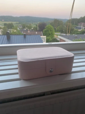 Ljusrosa smyckesbox i konstläder - Snygg och praktisk ljusrosa smyckesbox i konstläder med mjuk insida. Boxen har flera fack för ringar, örhängen och halsband samt en knappstängning. Perfekt för att organisera dina smycken hemma eller på resan.