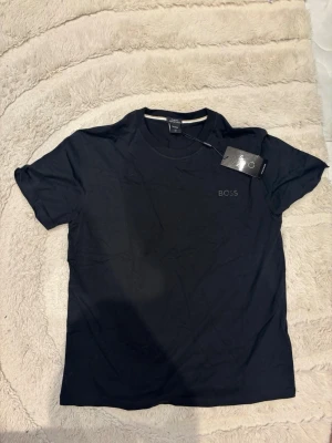 Svart BOSS t-shirt  - Svart t-shirt från BOSS med rund halsringning och korta ärmar. T-shirten har en stilren och diskret BOSS-logga på bröstet. Tillverkad i mjukt material som känns skönt mot huden. Perfekt för en clean och modern look.