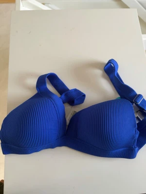 Blå ribbad bikiniöverdel - Snygg blå bikiniöverdel med ribbad struktur och vadderade kupor. Axelbanden är justerbara och har en knyt-detalj. Perfekt för strandhäng eller semester!