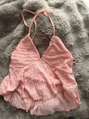 Ljusrosa halterneck topp - Supersöt ljusrosa halterneck topp med omlott-design och volangdetaljer som är köpt från SHEIN i storlek 44. Säljer den för jag tyckte inte den passade mig så bra. 