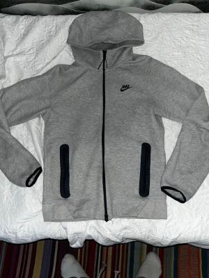 Grå Nike hoodie med dragkedja XS - Snygg grå hoodie från Nike med svart logga på bröstet och hel dragkedja framtill. Två svarta dragkedjeförsedda fickor och huva. Tillverkad i mjukt material som känns skönt mot huden. Perfekt för chill eller träning.