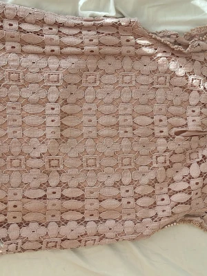 Rosa festtopp - Säljer en ljusrosa topp med vacker spets och volangkant. Toppen har ett unikt geometriskt spetsmönster och är fodrad undertill för extra komfort. Perfekt för dig som vill ha en feminin och trendig look.