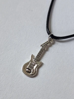 Halsband med elgitarr-hänge - Coolt halsband med ett silverfärgat elgitarr-hänge i metall. Hänget har detaljerade inslag som strängar och knappar, och hänger på ett svart, tunt band. Perfekt accessoar för dig som älskar musik och vill sticka ut med din stil.
