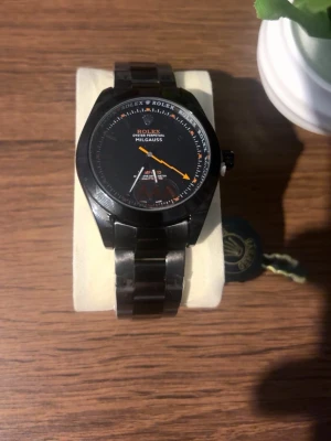Klocka - Klocka med svart urtavla och orange sekundvisare. Klockan har en robust länk i metall och tydliga vita markeringar på urtavlan. Perfekt accessoar för dig som gillar klassisk och stilren design. Priset kan diskuteras!