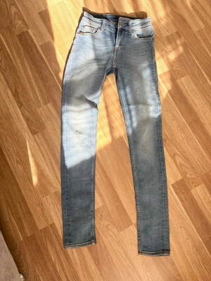 Tiger of Sweden Ljusblå skinny jeans med slitningar - Säljer ett par ljusblå skinny jeans med klassisk femficksdesign och snygga slitningar framtill. Jeansen har kontrastsömmar och en läderpatch bak i midjan. Materialet är stretchigt denim som sitter tight längs benen. Perfekta för en avslappnad och trendig look.