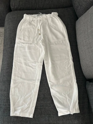 Vita linnebyxor från Zara - Säljer ett par vita linnebyxor från Zara med avslappnad passform och resår i midjan med dragsko. Byxorna har två stora fickor fram och är perfekta för en chill och stilren look. Materialet är luftigt linne som passar perfekt till sommaren.