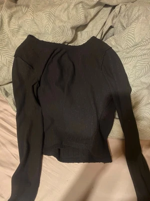 Svart långärmad topp - En svart, figurnära långärmad topp med rund halsringning och ribbad nederkant. Toppen har en enkel och stilren design som passar till många olika outfits. Materialet ser ut att vara mjukt och stretchigt, perfekt för en trendig vardagslook.
