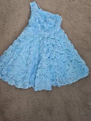 Ljusblå axelbandslös klänning Faeriesty - Supersöt ljusblå axelbandslös klänning från Faeriesty, täckt med 3D-blommor som ger en unik och romantisk look. Klänningen har en kort, utsvängd modell och är perfekt för dig som vill sticka ut. Materialet känns mjukt och lätt mot huden.