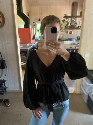 Svart långärmad blus - Säljer denna svarta v-ringade blus.  Har knytband som man knyter själv, går även att ta bort bandet.  Vid armarna går den in. Resor i midja och ärmar.  Storlek S.