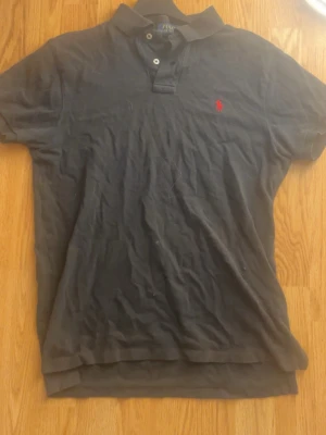 Svart pikétröja med röd logga - Säljer nu min svarta Ralph lauren Piké (slim fit) storlek M!  Anledning? Den är lite för kort för mig. Tagit hand om den väl och använd bara på speciella dagar. Ralph lauren loggan ligger som vanligt på bröstet i färgen röd.  Pris? 350kr men går såklart att diskuteras me rimlig mängd!   Nyfiken eller vill ha mer bilder? Hör av dig!
