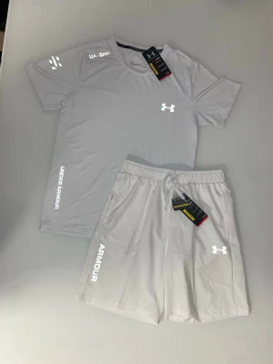 Under Armour set Vit - Snyggt och sportigt set från Under Armour med t-shirt och matchande shorts. Perfekt för gym, träning eller vardag.  Båda plaggen är helt nya med tags, aldrig använda. Lätt och bekvämt material med reflexdetaljer – perfekt för både träning och stil.  ✔️ Skick: Helt nya (med tags) ✔️ Set: T-shirt + shorts ✔️ Passform: Sportig och bekväm M/S ✔️ Perfekt för gym, löpning eller vardag och perfekt för sommaren!  Riktigt clean set 🔥