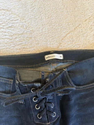 Bootcut jeans med snörning, Perfect Jeans - Mörkblå bootcut jeans från Perfect Jeans i storlek 38. De har cool snörning framtill istället för vanlig dragkedja och fickor både fram och bak. Jeansen är tillverkade i denim med snygga slitningar på låren och har en trendig utsvängd passform.