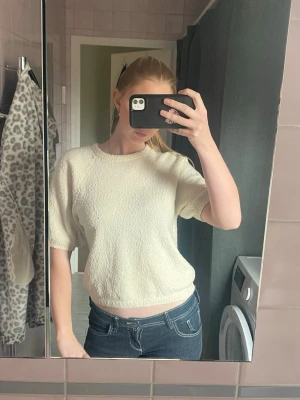 Creme vit topp - Säljer en vit topp med korta ärmar och rund hals. Toppen har en lätt strukturerad yta och en avslappnad passform som slutar vid  höften. Tröjan är i storlek M, men jag själv skulle säga att den passar S också.💗