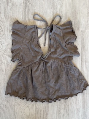 Beige topp från Lager 157 - Supersöt beige topp från Lager 157 i storlek XS. Toppen har volangdetaljer på ärmarna, knytning i nacken och en djup v-ringning framtill. Materialet är lätt och skönt, perfekt för varma dagar. Den har en loose passform och är riktigt trendig💜Kolla in min profil för fler fina och trendiga plagg!