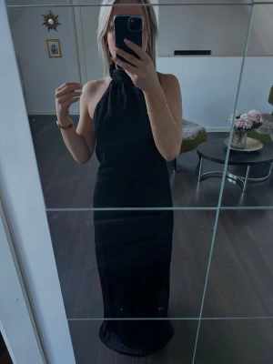 Svart långklänning med öppen rygg - Säljer en svart satin långklänning (balklänning) med halterneck och öppen rygg, från peppermayo. Helt ny och oanvänd och säljs pga hittade en annan till min bal. Nypris 1400kr. Storlek 36 (S).