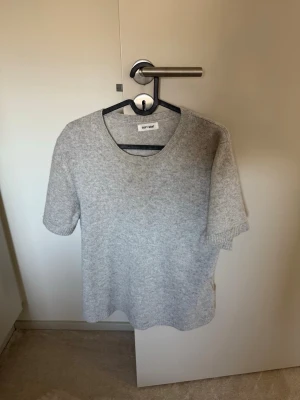 Grå stickad t-shirt från Soft Goat - Säljer en stilren grå stickad t-shirt från Soft Goat. Tröjan har korta ärmar, rund halsringning och är gjord i mjukt material, troligtvis kashmir. Perfekt för en avslappnad men snygg look.