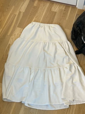 Vit långkjol med volanger - Säljer en vit långkjol med volangdetaljer. Kjolen har en avslappnad passform och resår i midjan för extra komfort. Perfekt för dig som gillar en enkel men stilren look.