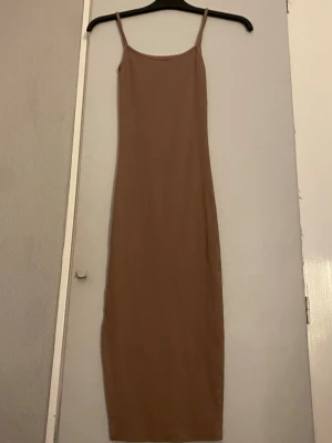 Puderrosa långklänning med smala axelband - En enkel och stilren puderrosa långklänning med smala axelband och rak passform. Klänningen har ett minimalistiskt uttryck och passar perfekt för dig som gillar en clean look. Materialet känns mjukt och lätt, vilket gör den bekväm att bära.