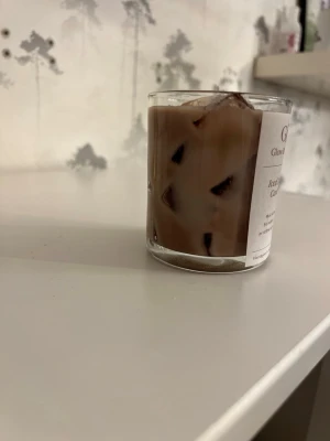Doftljus iskaffe - Unikt doftljus i glas som är designat för att likna ett glas iskaffe med isbitar. Ljusets färg är brun med genomskinliga detaljer som imiterar is. Perfekt för dig som gillar roliga och annorlunda inredningsdetaljer. Mjuk doft av kaffe