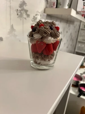 Dekorativ doftljus glasdessert med jordgubbar - Säljer en dekorativ doftljus i form av glasdessert som ser ut som en efterrätt med röda jordgubbar, vit och brun grädde samt hallon och blåbär. Doft av olika bär