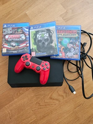 PlayStation 4 med röd handkontroll - Säljer en svart PlayStation 4-konsol från Sony tillsammans med en röd DualShock 4-handkontroll. Medföljer gör även tre PS4-spel: Pinball Arcade, Call of Duty och Transformers Battlegrounds. Konsolen har en stilren, rektangulär form och är tillverkad i plast.