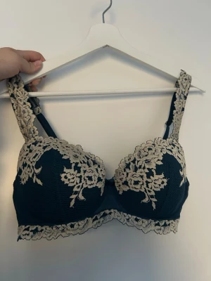 Intimissimi bh  - Snygg svart bh med vadderade kupor och vackra beige spetsdetaljer över kuporna, axelbanden och nedtill. Bh:n har en feminin design med blommönstrad spets och breda axelband för extra komfort. Perfekt för dig som gillar en elegant och stilren look.