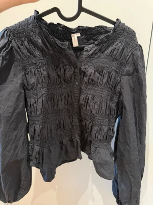 Svart blus från Nelly  - Säljer denna svarta blus från Nelly. Det är deras Flirty Smock Blouse som inte säljs längre. Den är i storlek 38 men jag skulle säga att den är mer storlek 36/34 då den är väldigt kort💕 om du har några frågor är det bara att höra av dig