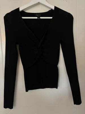 Svart ribbad topp med knut - Svart långärmad topp från River Island med ribbat material och snygg design framtill. Jättesnygg form och passar perfekt till vardags eller fest!! Använd 1 gång. Nypris är 500kr.
