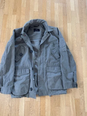 Tiger of Sweden Overshirt - Snygg olivgrön jacka från Tiger of Sweden med fyra stora fickor framtill och knappstängning. Jackan har klassisk krage och är tillverkad i ett slitstarkt bomullstyg. Perfekt för dig som gillar en avslappnad men stilren look.