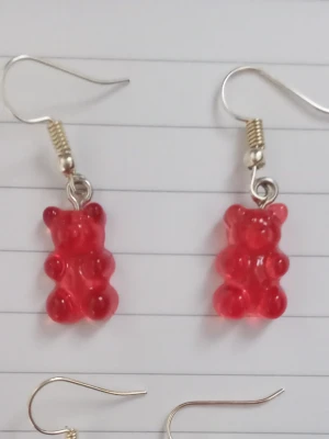Röda björn örhängen - Säljer ett par unika örhängen med röda gummibjörns-hängen i plast. Örhängena har krokar i metall och är knappt använda. 