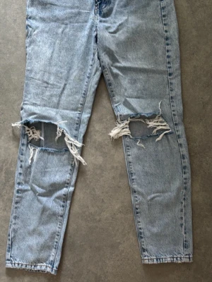 Ljusblå ripped jeans från g perfect jeans - Säljer ett par ljusblå jeans från g perfect jeans med stora slitningar över knäna. Klassisk femficksmodell med dragkedja och knapp. Perfekt för dig som gillar en avslappnad och trendig stil.