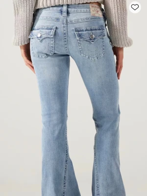 Ljusblå bootcut jeans True Religion - Säljer ett par ljusblå bootcut jeans från True Religion med ikoniska fickor bak, silverfärgade knappar och klassisk patch i midjan. Jeansen har en snygg tvätt och är tillverkade i mjuk denim med lätt stretch. Perfekta för en avslappnad men trendig look.