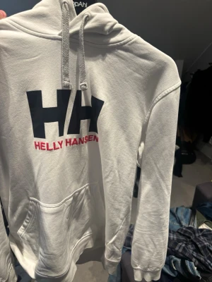 Vit hoodie från Helly Hansen - Vit hoodie från Helly Hansen. Klassisk huva med grå snören och mjukt foder. Stora fickor framtill och ribbade muddar vid ärmslut och nederkant. Använt fåtal gånger. Storlek L sitter nog bättre på M