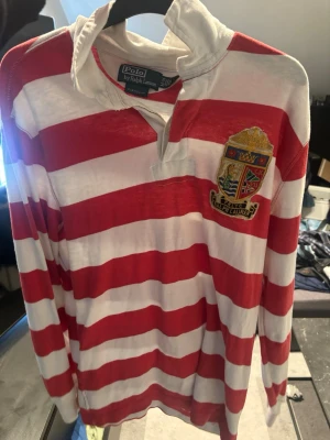 Rödvit randig Polo Ralph Lauren piké  - En väldigt gammal o nischad Rugbytröja med breda röda och vita ränder från Polo Ralph Lauren. Materialet är mjukt och bekvämt, perfekt för en avslappnad stil. Använd ytterst sällan. 