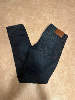 Mörkblå slim fit jeans från Jack & Jones - Snygga mörkblå slim fit jeans från Jack & Jones  storlek 29/30 med klassisk femficksdesign och läderpatch bak i midjan. Jeansen har en smal passform och är tillverkade i denim med lätt stretch för extra komfort.