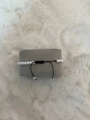 Vitt pärlarmband med justerbart band - Snyggt armband med vita runda pärlor trädda på en svart justerbar tråd. Perfekt för dig som gillar enkel och stilren design. Passar till många olika outfits och är lätt att ta på och av tack vare det smidiga knytbandet.