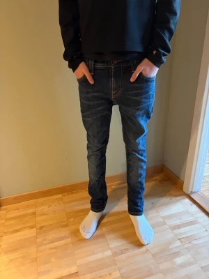 Mörkblå slim fit jeans från Nudie - Säljer ett par mörkblå slim fit jeans från Nudie Jeans med klassiska kontrastsömmar och broderade bakfickor. Jeansen har normal midja, fem fickor och är tillverkade i stretchig denim för skön passform.