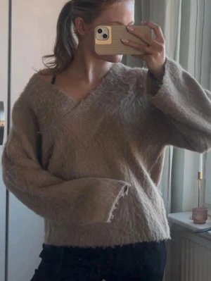 Beige oversized stickad tröja - Mysig beige stickad tröja med v-ringning och breda ärmar. Tröjan har en avslappnad, oversized passform och är tillverkad i ett fluffigt, mjukt material som känns skönt mot huden. Perfekt för lager-på-lager och chill dagar.