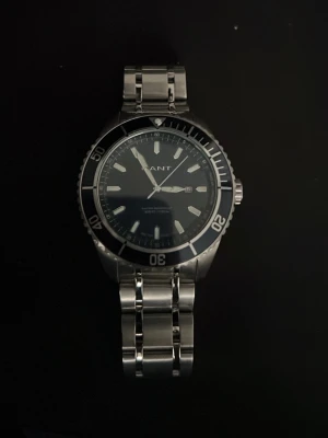 Stilren klocka från Gant i stål - Snygg klocka från Gant med svart urtavla och datumvisning. Boetten och länken är i rostfritt stål och har en sportig känsla med vridbar bezel och tydliga markeringar. Perfekt accessoar för dig som gillar klassisk men modern stil. Urladdat batteri! Nypris 2100kr, mitt pris 900kr. Kom med bud!