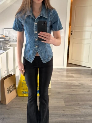 Blå jeans topp Gina Tricot  - Snygg blå denimblus med korta ärmar och markerad midja. Blusen har klassisk krage, tydliga sömmar och knappar hela vägen framtill. Endast använd ett fåtal gånger så den är i mycket bra skick!
