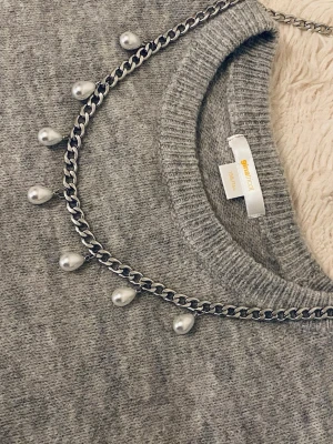 Silverfärgat halsband med pärlor - Snyggt halsband med en kraftig silverfärgad rostfritt stål kedja och droppformade vita pärlor som hänger längs hela kedjan. Perfekt för dig som vill ha en cool och trendig accessoar med lite extra detaljer. Passar till många olika outfits och ger en unik touch.